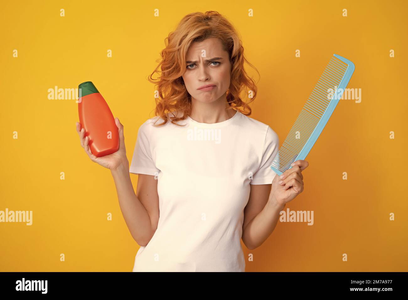 Angry sad woman hairdresser with comb. Funny woman hold bottle shampoo and conditioner. Girl combing hair. Redhead woman with a comb, isolated on Stock Photo