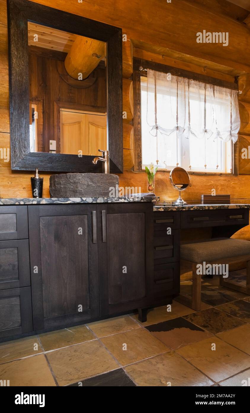 Charcoal wooden vanity with sink made from crushed river stones glued together with epoxy and makeup table in bathroom inside luxurious log home. Stock Photo