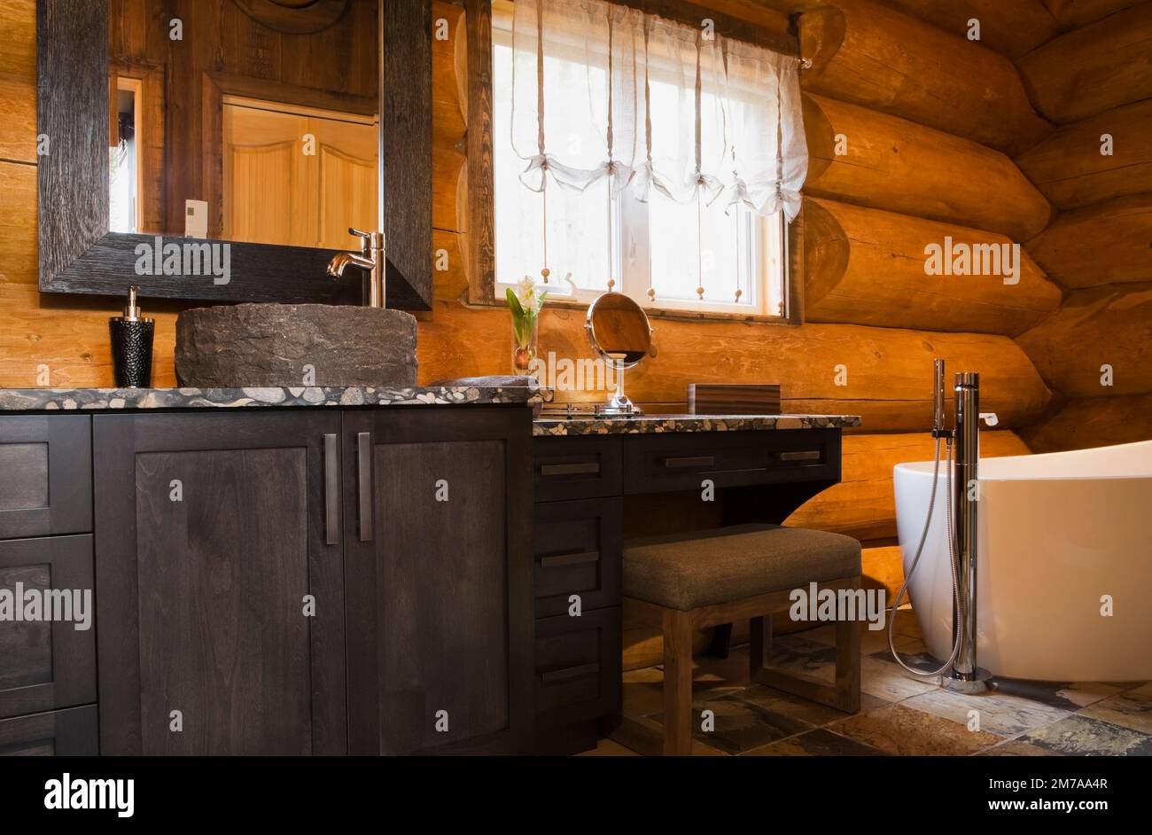 Charcoal wooden vanity with sink made from crushed river stones glued together with epoxy and white freestanding oval bathtub in bathroom. Stock Photo
