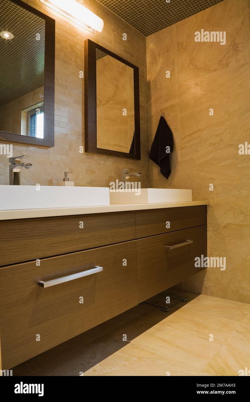 White rectangular porcelain sinks and brown wooden vanity in his and her bathroom on upstairs floor inside modern cubist style home. Stock Photo