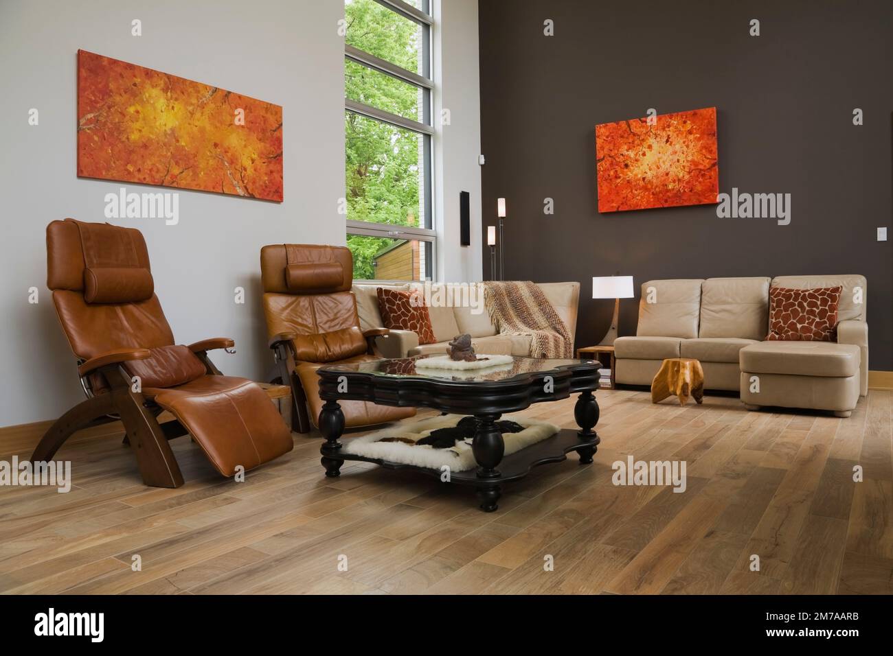 Caramel leather high back reclining armchairs and tan sofas with black wooden glass top coffee table in living room inside modern cubist style home. Stock Photo