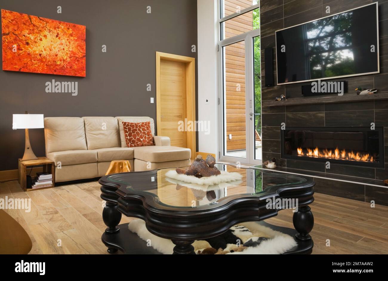 Tan leather sofa and black wooden glass top coffee table with lit gas fireplace in living room inside modern cubist style home. Stock Photo