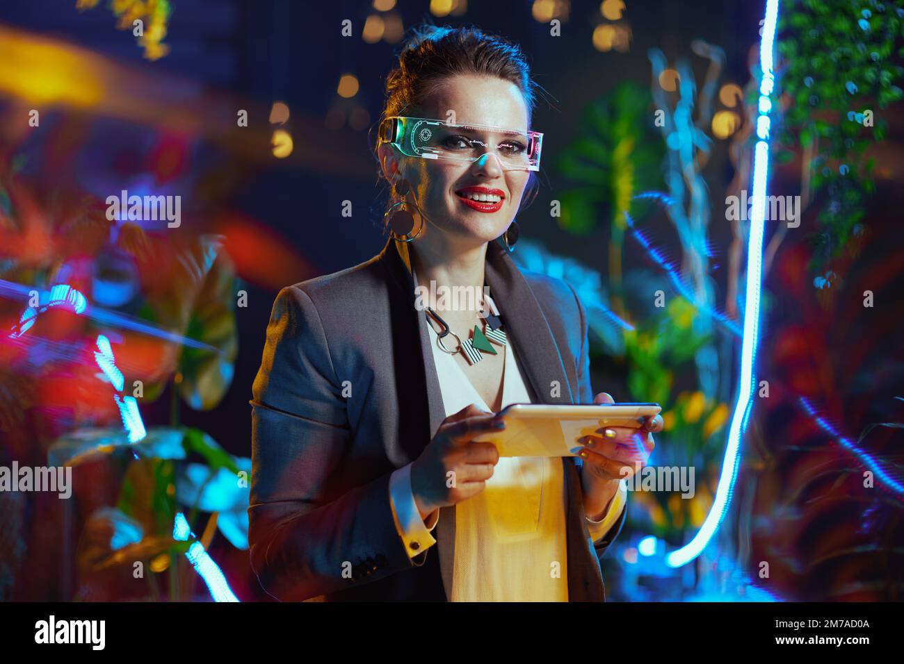 Portrait of happy modern business woman with futuristic goggles using tablet PC in metaverse. Stock Photo