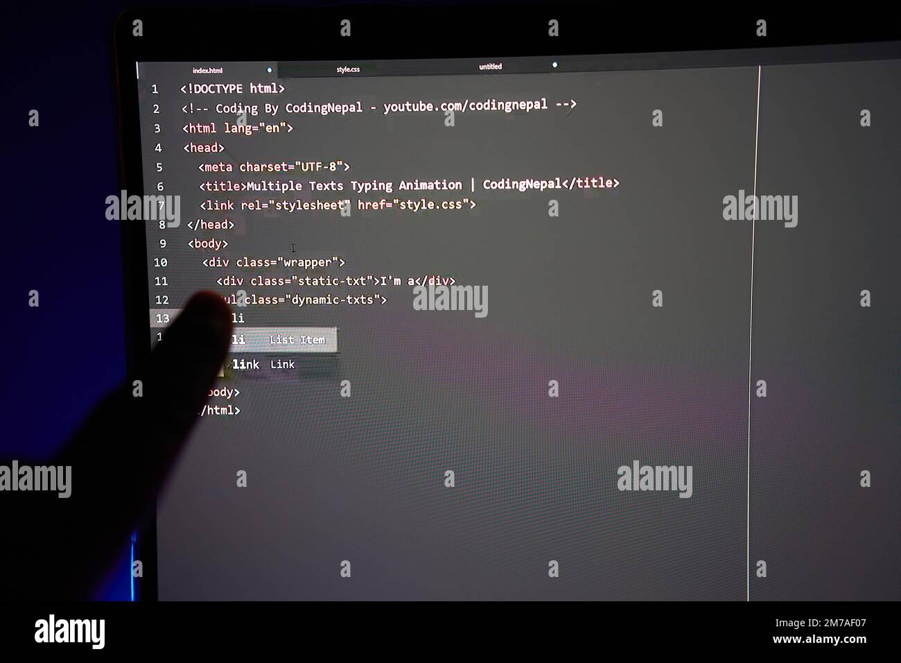 Writing computer code displayed on monitor pointing finger at a line of ...