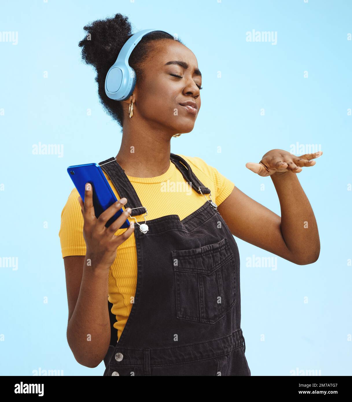 Black woman, music and phone in studio with dance, dj hand gesture and listening by blue background. Gen z girl, streaming audio or online radio on Stock Photo