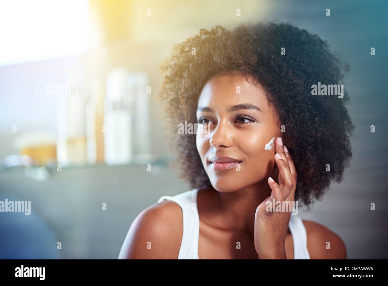 Thinking about skincare. a young woman moisturizing her face in the bathroom. Stock Photo