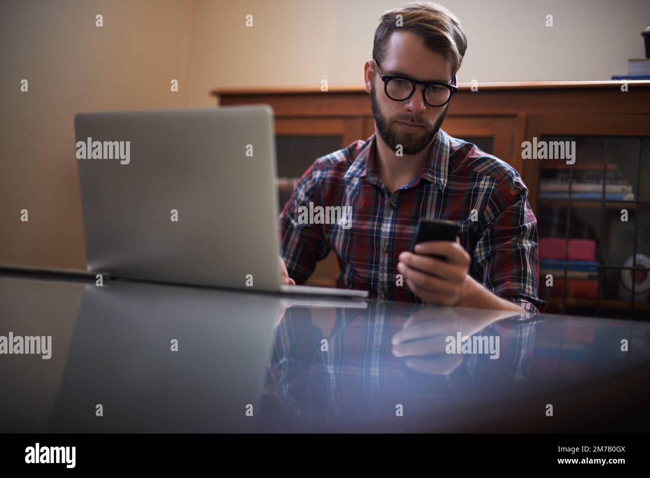 Using all the latest tech. a handsome young hipster working on a laptop. Stock Photo