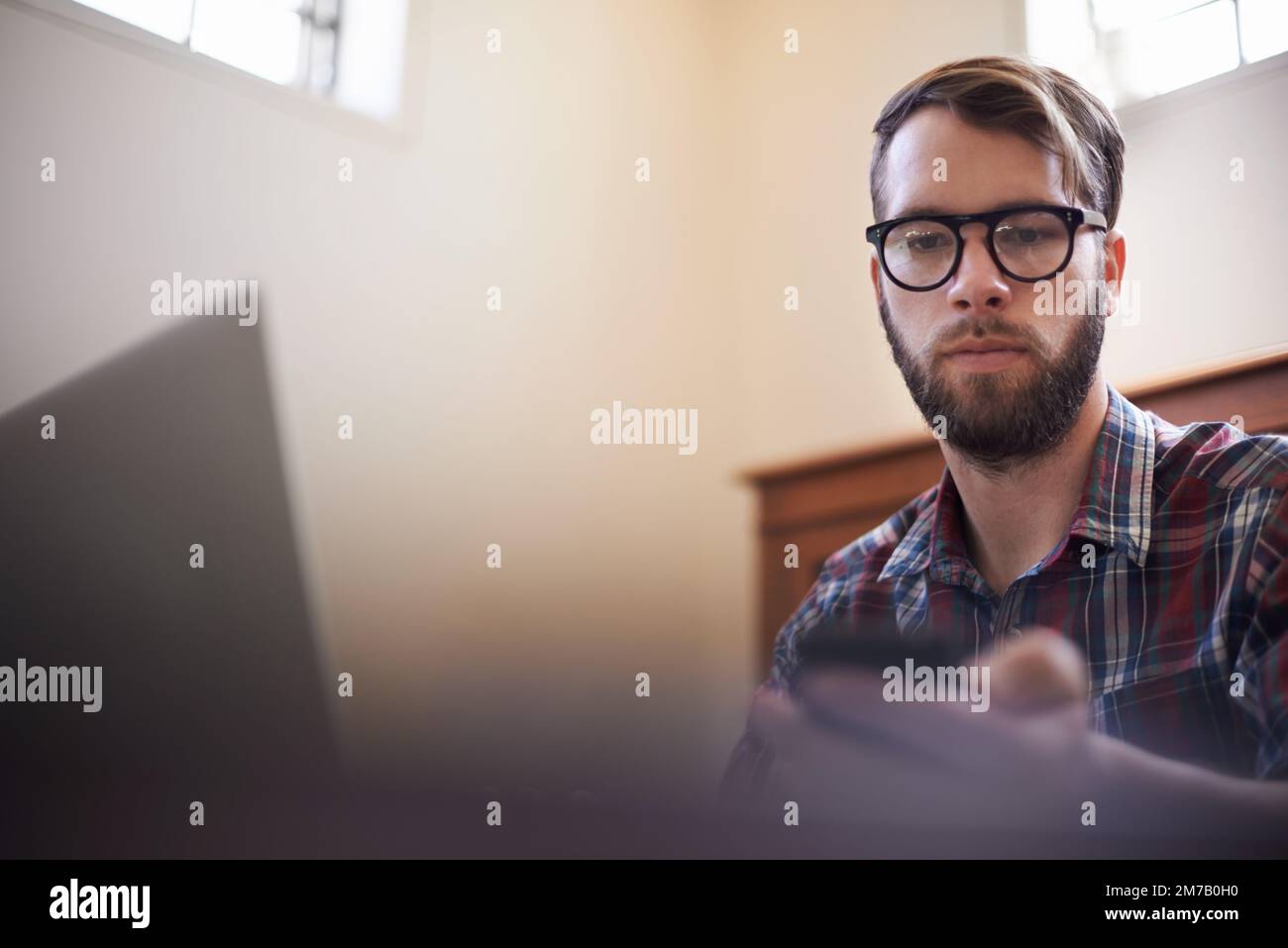 Using all the latest tech. a handsome young hipster working on a laptop. Stock Photo