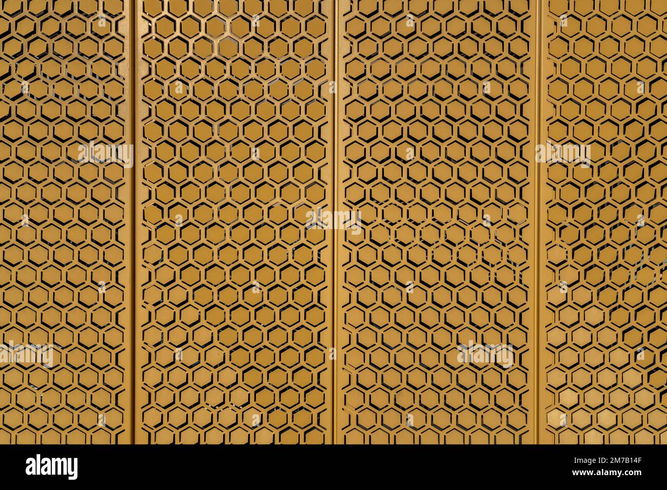 Detail of yellow ochre metal plates with hexagonal pattern covering building wall - bright background in sunlight Stock Photo