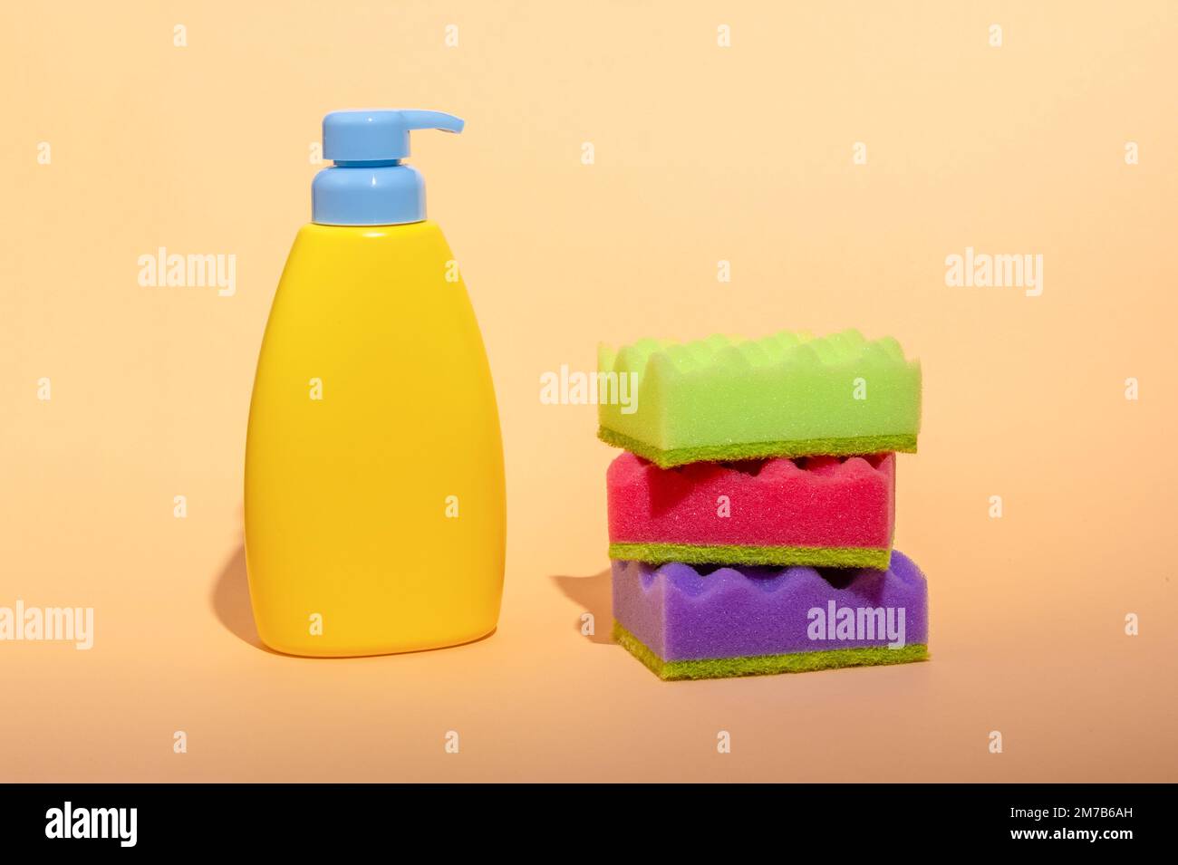 Stack of multi-colored dish wash sponges with bottle of soap on pastel orange background. Household cleaning scrub pad. Home cleaning concept. Stock Photo