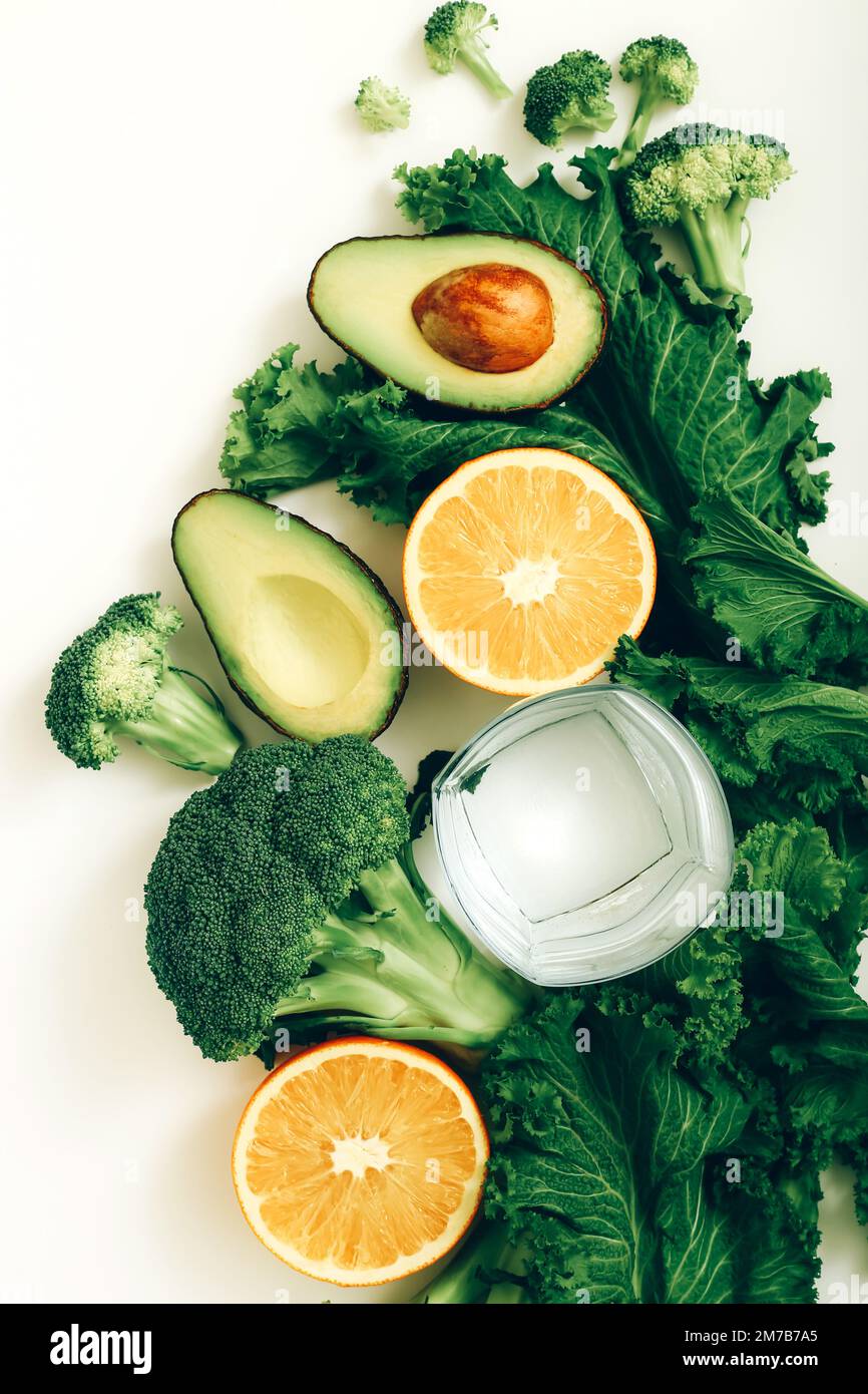 Glass of pure water, avocado, broccoli, orange and lettuce on the white table. Healthy lifestyle and diet concept. Stock Photo