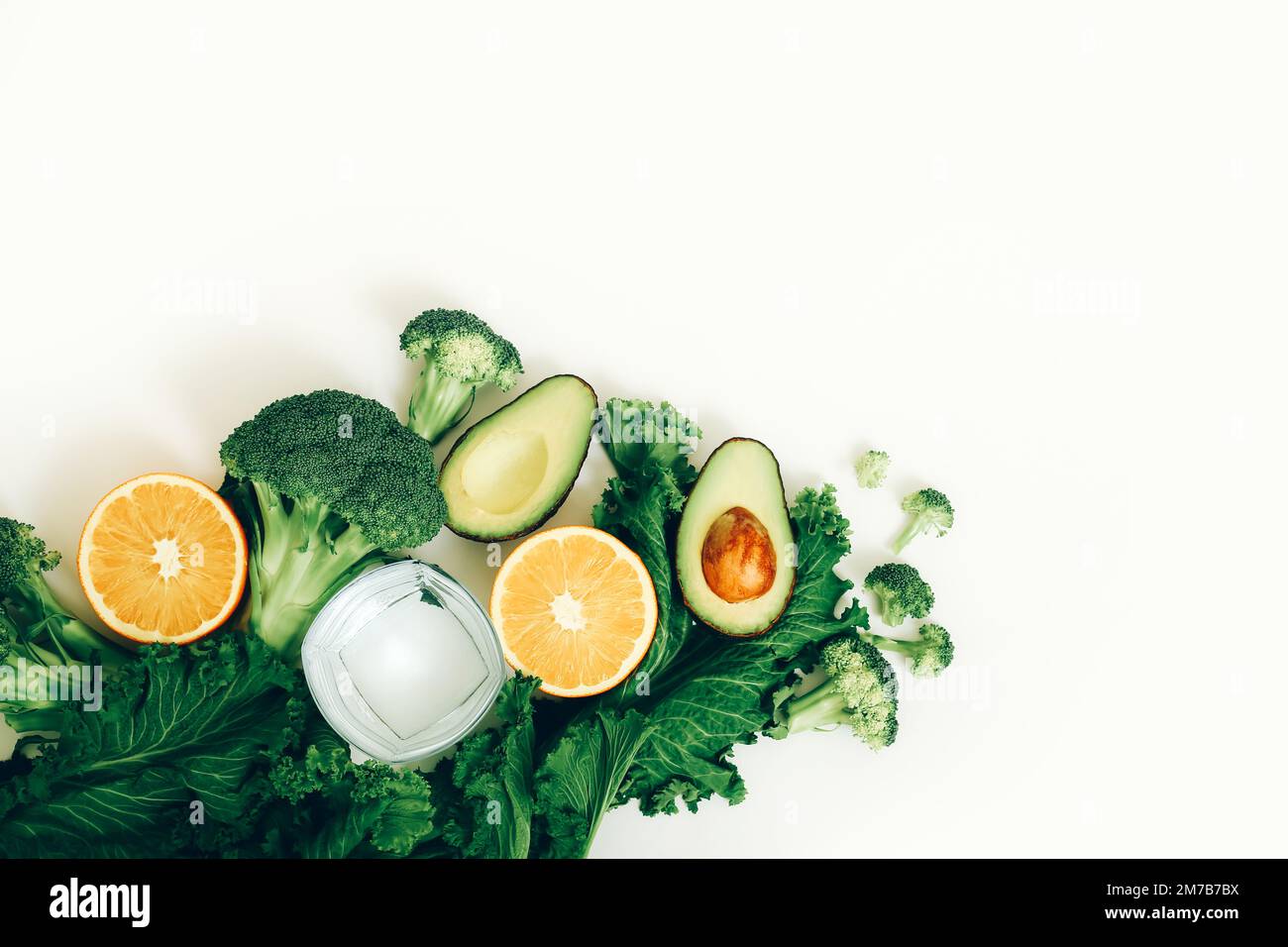 Glass of pure water, avocado, broccoli, orange and lettuce on the white table. Healthy lifestyle and diet concept. Stock Photo