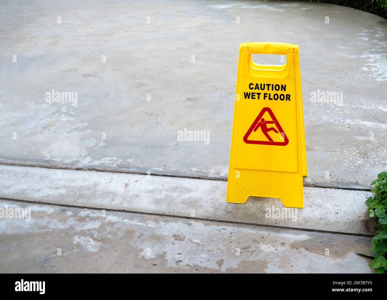 Yellow caution slippery wet floor sign with slippery person warning icon on wet concrete floor background after raining with copy space. Stock Photo