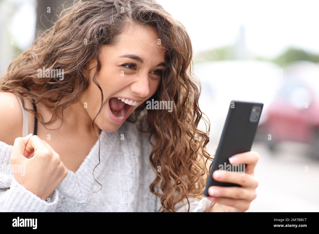 Excited woman celebrating checking phone in the street Stock Photo