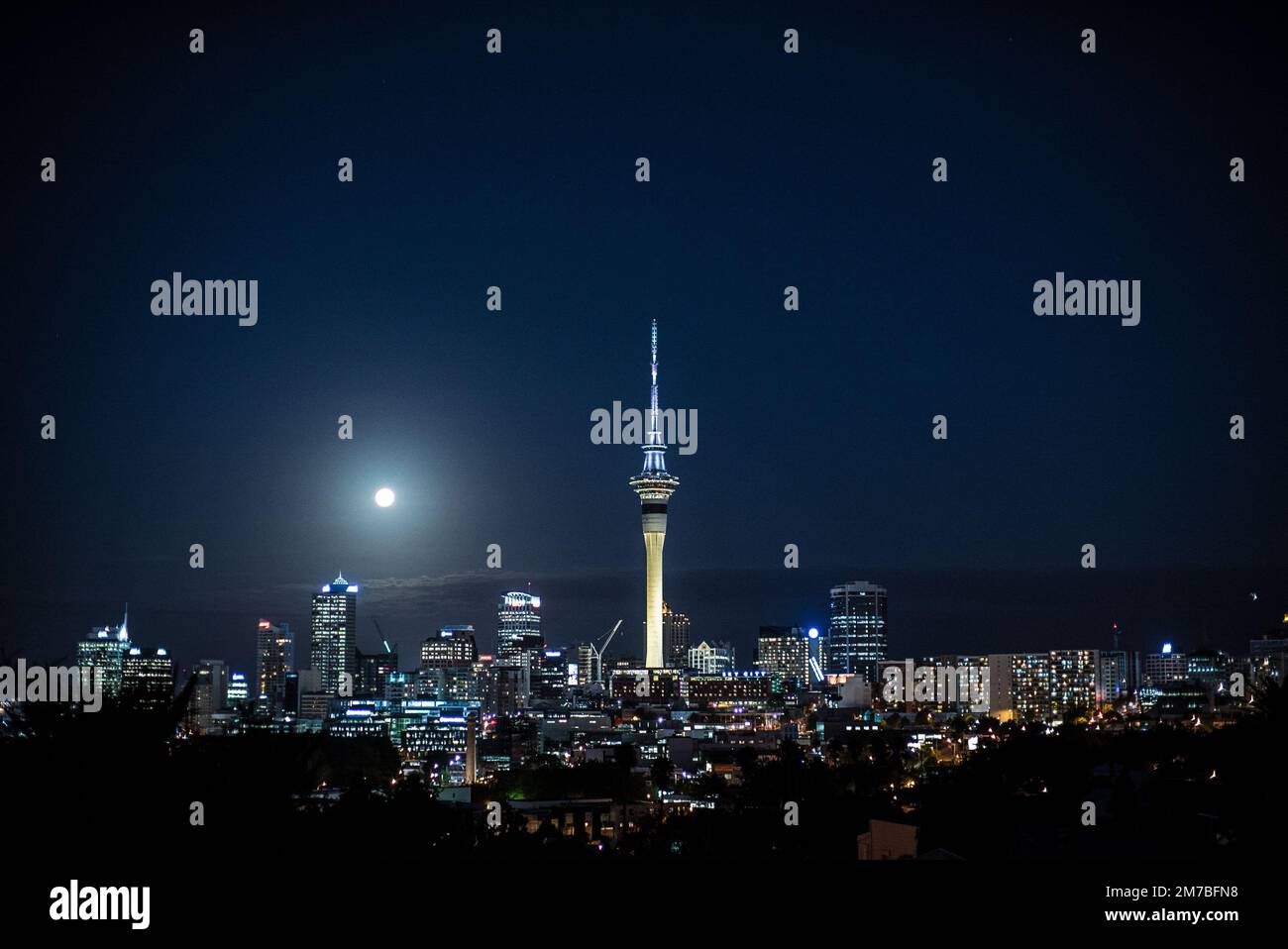 The skyline of Auckland with illuminated buildings and the full moon in