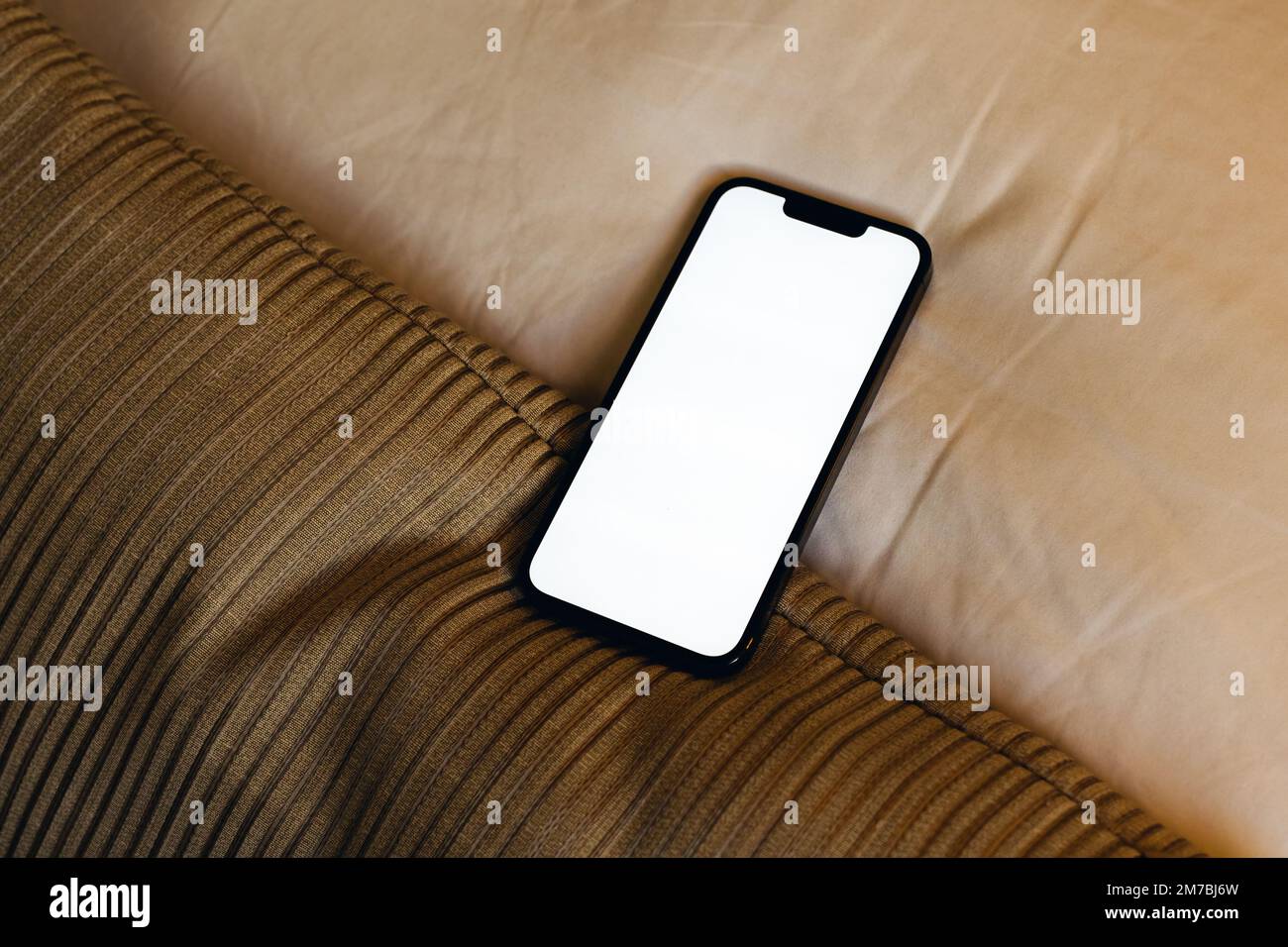 Smartphone with blank white screen as mockup copy space on bed sheet