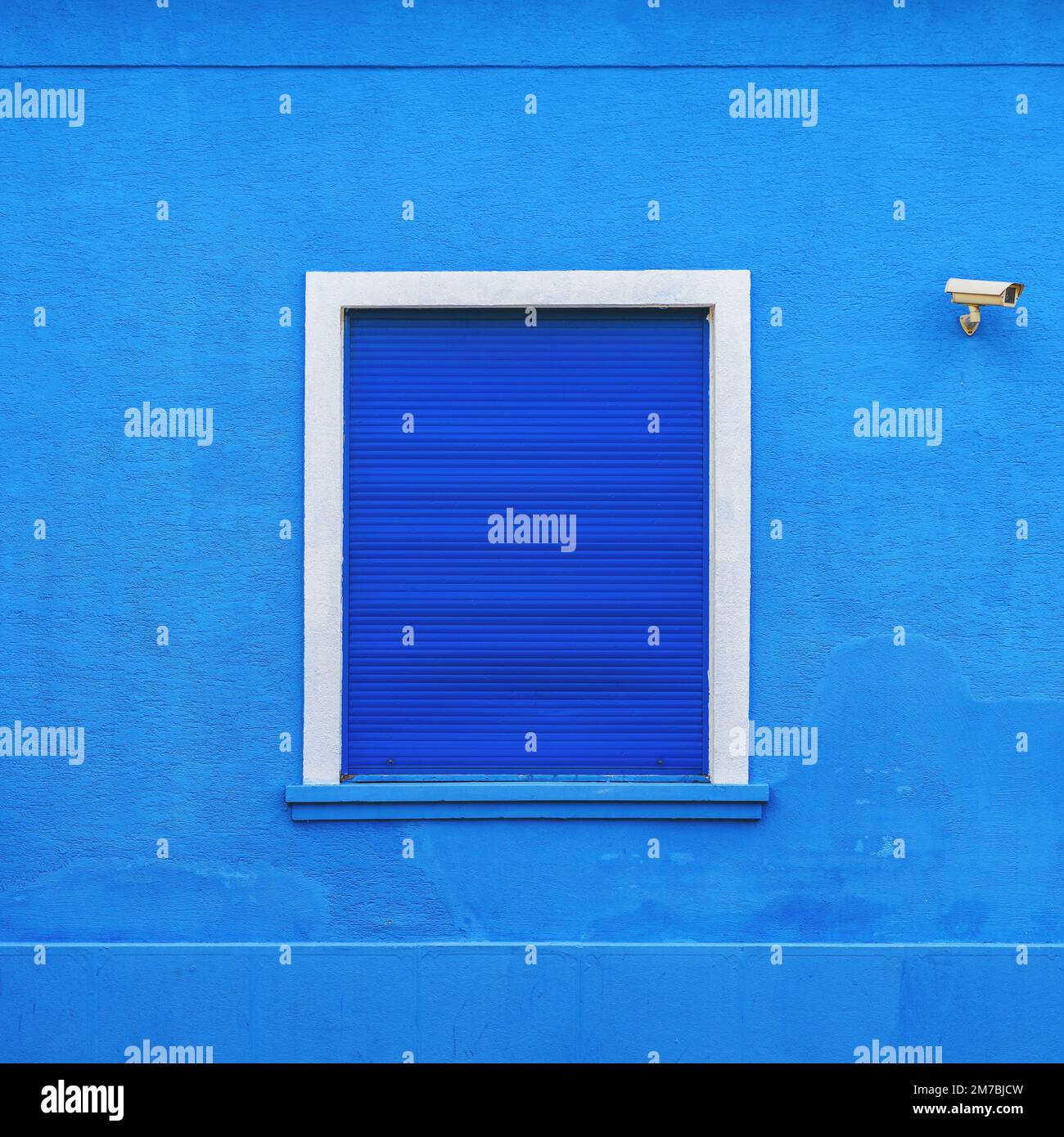Window on blue facade with dark blue rolling shutters and security camera Stock Photo