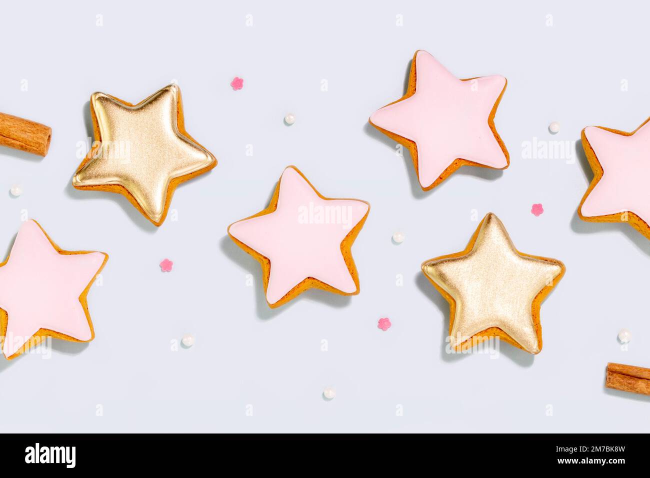 Holiday ginger cookies in the form of stars glazed sugar icing decoration on blue background with cinnamon sticks and topping for baking. Flat lay Stock Photo