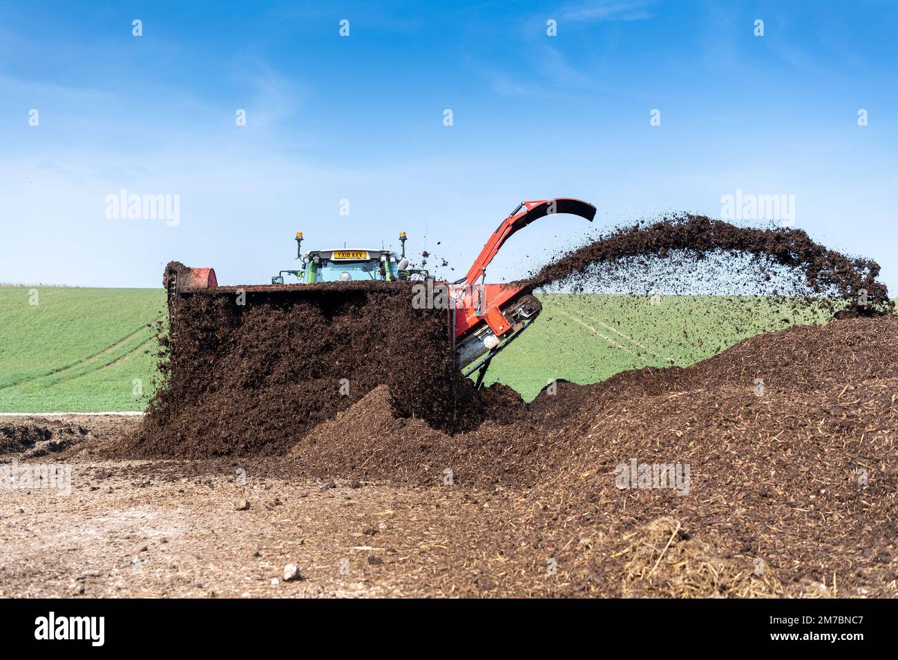 Turning a manure heap over to make compost to spread on farmland, which helps increase the