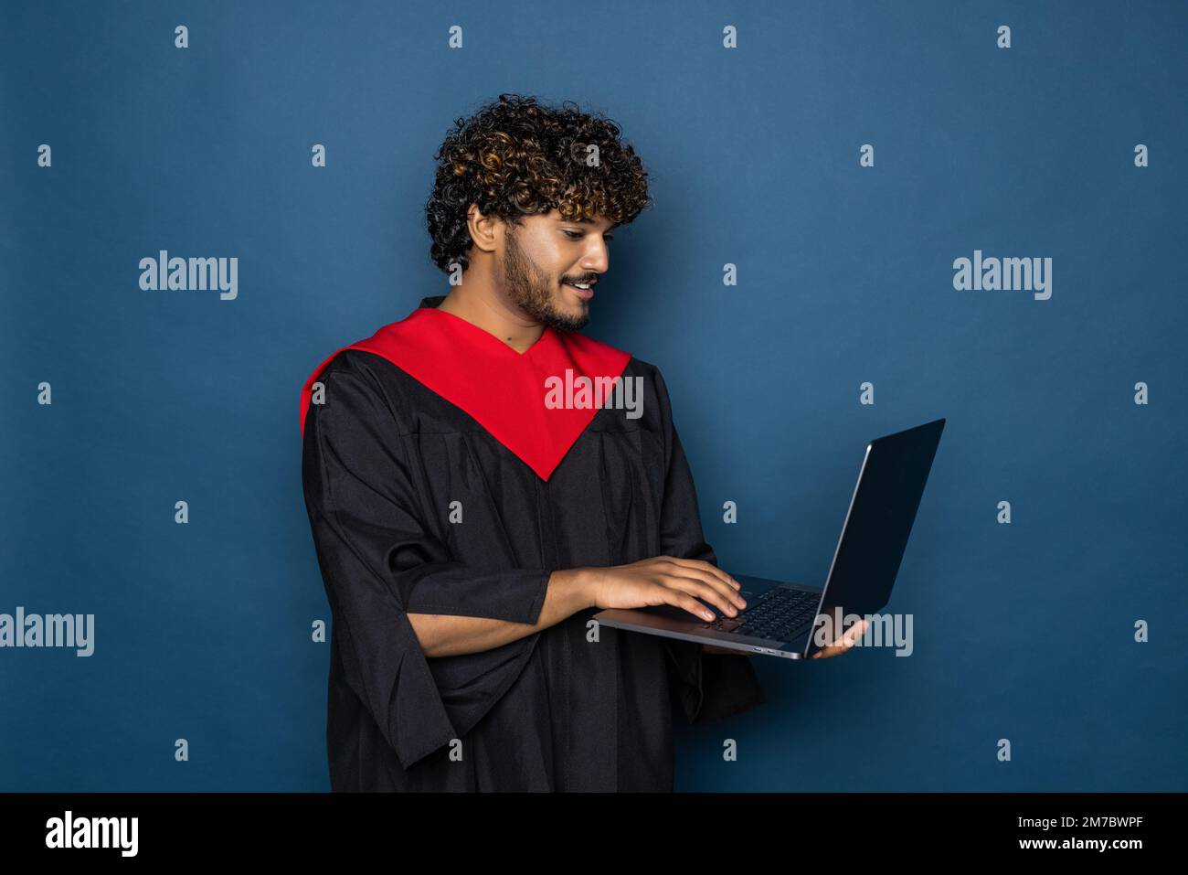 Male graduate holding a laptop computer and smiling at the camera ...