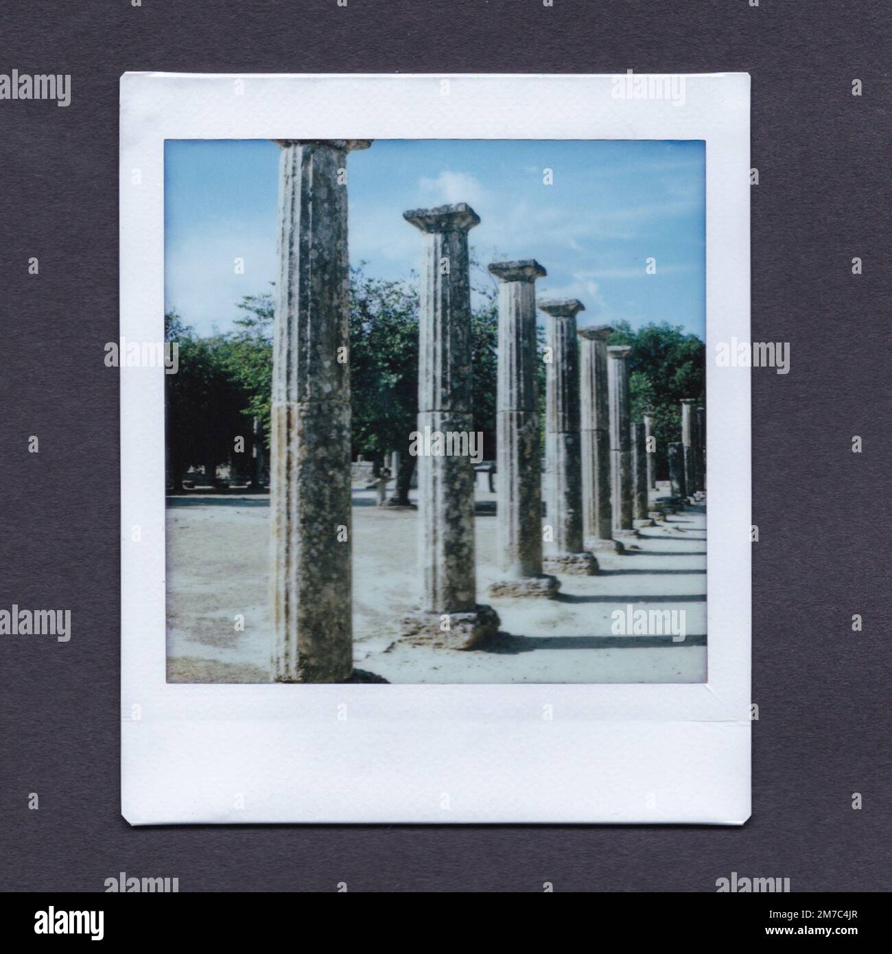 Instax photograph of columns leading to the distance in the archaeological site at Ancient Olympia, Greece. The Instax print is on a grey background. Stock Photo