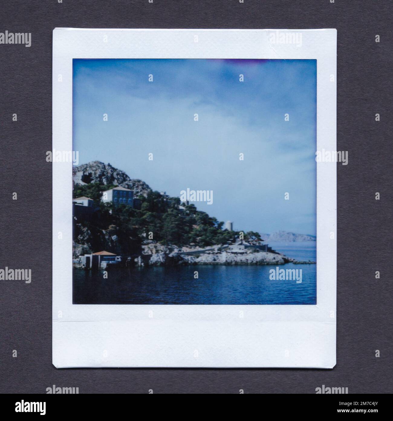 Instax photograph of Hydra, Greece. Photograph of an Instax print showing the island of Hydra with blue and lightly cloudy sky. Stock Photo