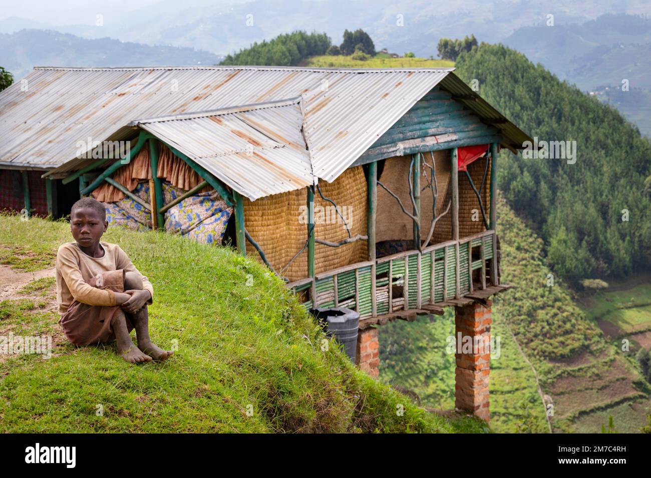 A young local girl sits by a dwelling in the subsistence farmland close to the Bwindi Impenetrable Rainforest National Park, south western Uganda. Stock Photo