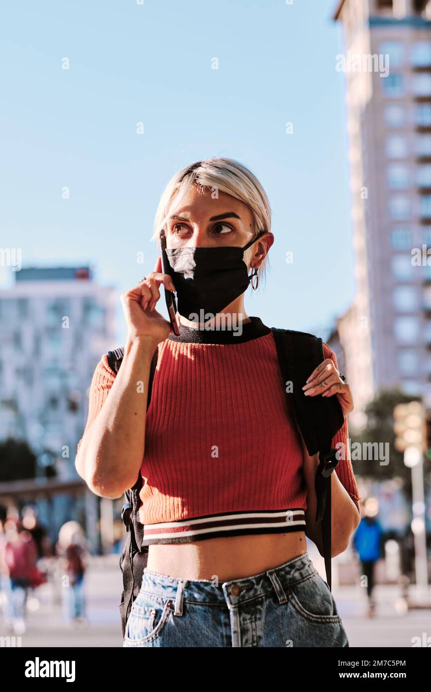 Woman with face mask talking on the phone while walking on the street. Stock Photo
