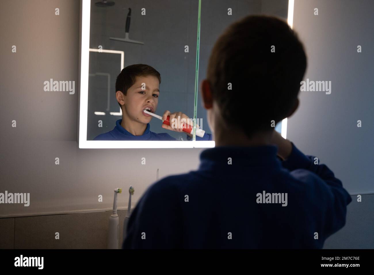 9 year-old boy (model released) cleaning his teeth using an electric tooth brush in the bathroom mirror before going to school, London, England UK Stock Photo