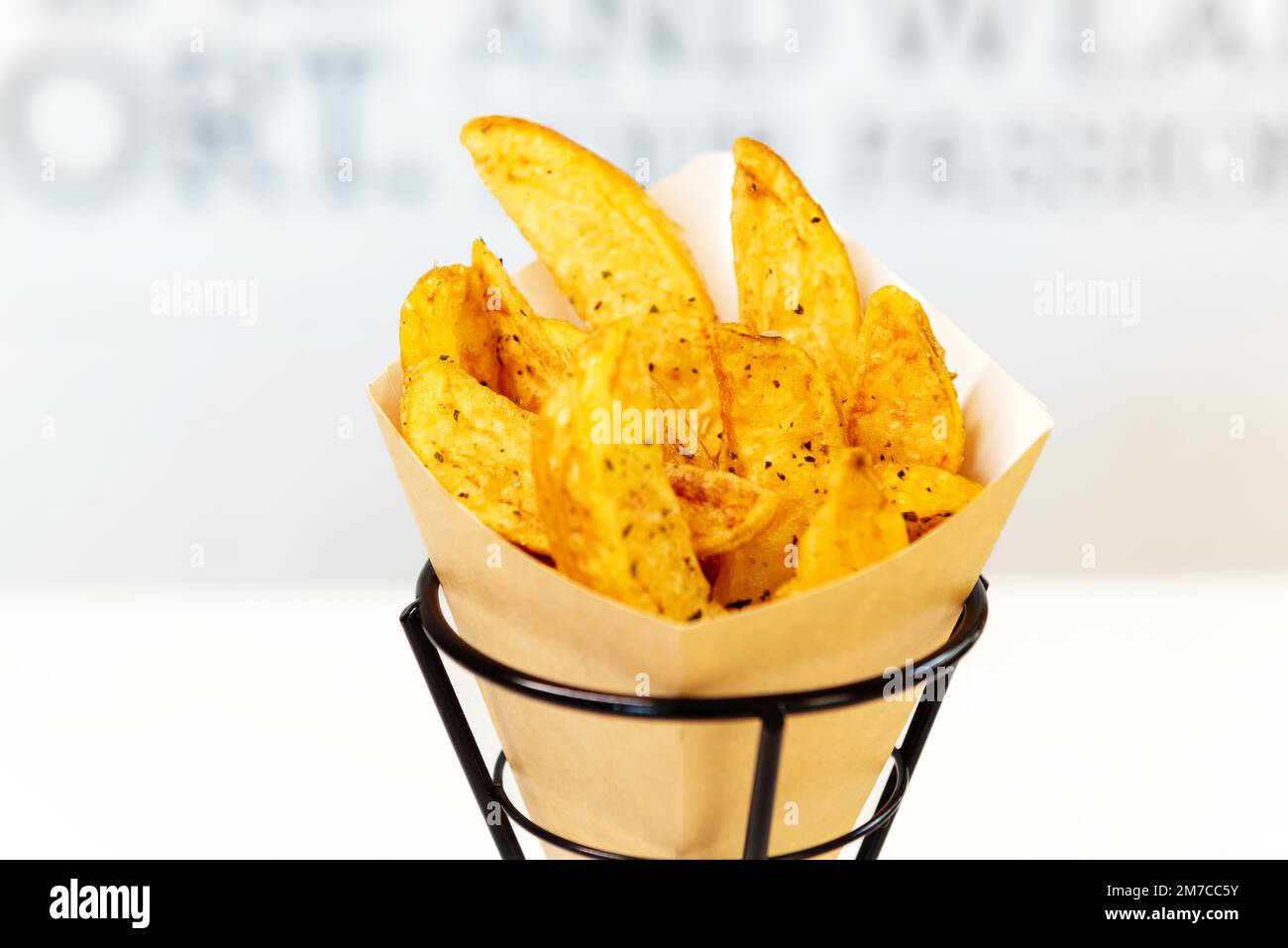 Oven baked potato wedges with sea salt and herbs. fries in a recyclable paper bag, popular fast street food Stock Photo