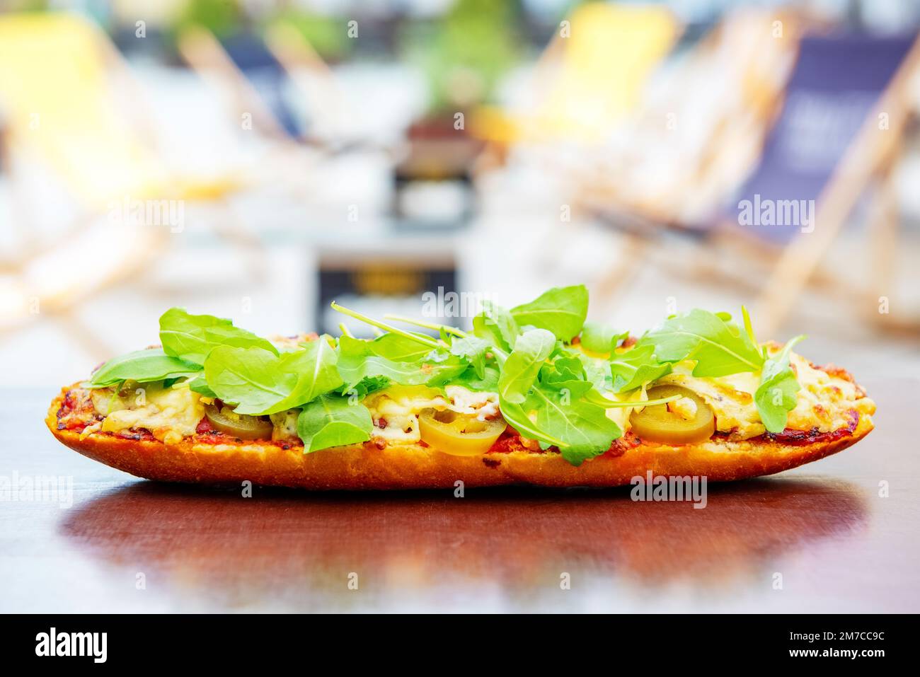 baguette with tomato sauce, meat, jalapeno and arugula baked with cheese on a table outdoor. popular street fast food Stock Photo