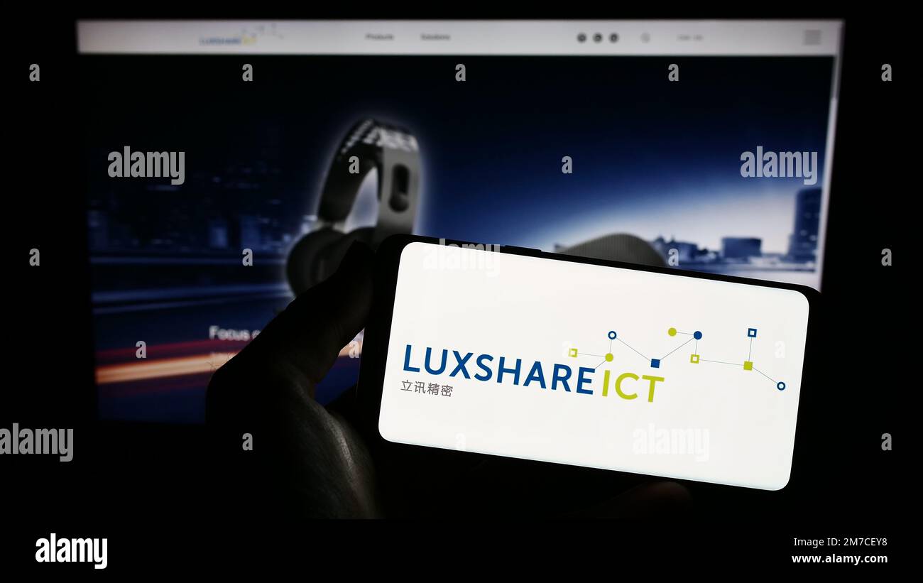 Person holding smartphone with logo of company Luxshare Precision Industry Co. Ltd. on screen in front of website. Focus on phone display. Stock Photo