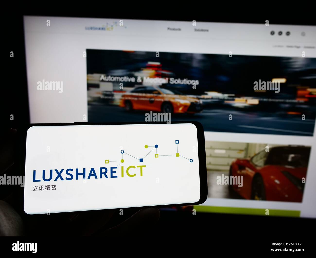 Person holding cellphone with logo of company Luxshare Precision Industry Co. Ltd. on screen in front of webpage. Focus on phone display. Stock Photo