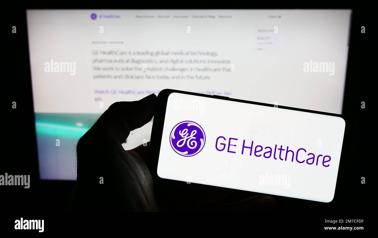 Person holding mobile phone with logo of American company GE HealthCare Technologies Inc. on screen in front of web page. Focus on phone display. Stock Photo