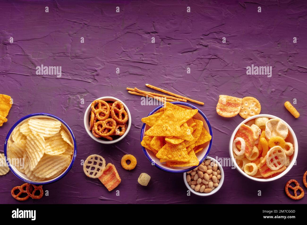 Salty snacks with a place for text. Party food. Potato chips, nachos, crackers and other appetizers in bowls, shot from the top Stock Photo