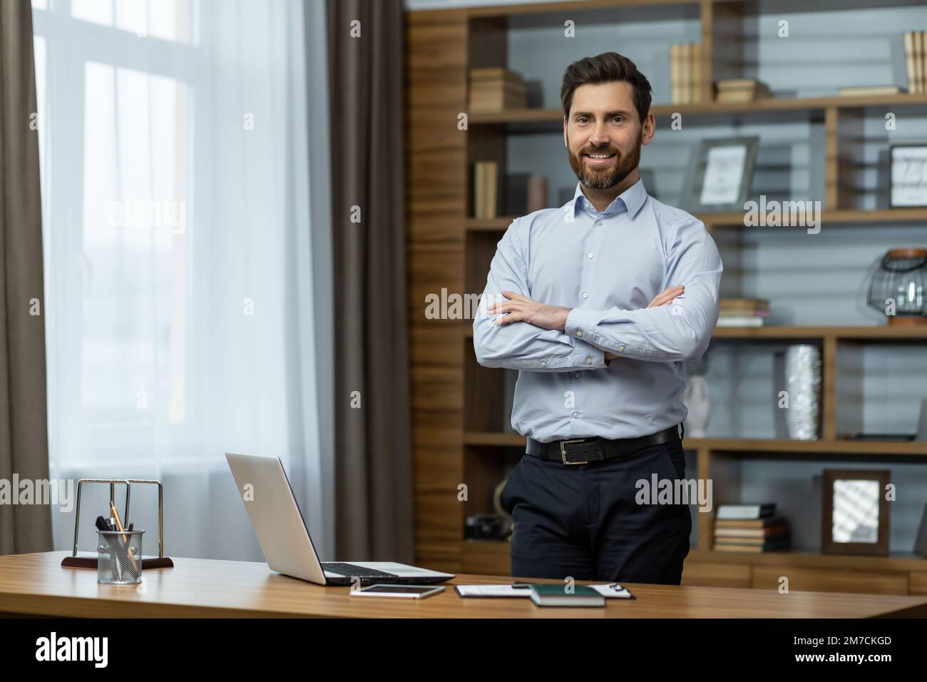Portrait of successful businessman in office, man in shirt smiling and looking at camera, mature boss with beard with shaggy hands standing at workplace inside building. Stock Photo