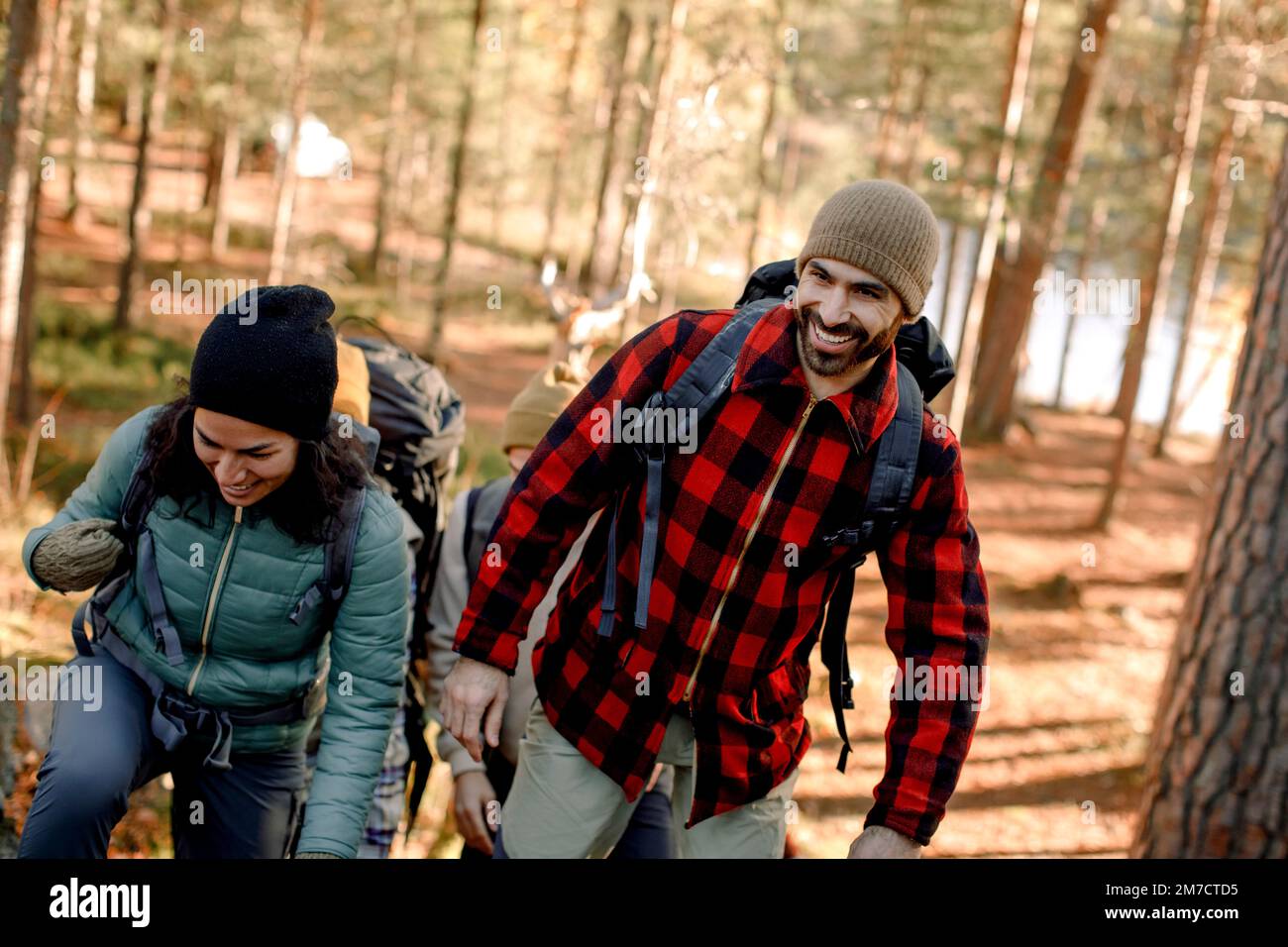 Happy man wearing plaid shirt while hiking with female friend in forest Stock Photo