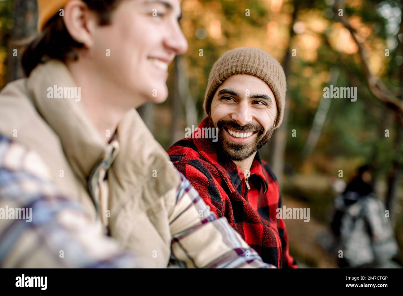 Happy man wearing plaid shirt talking to male friend during camping Stock Photo