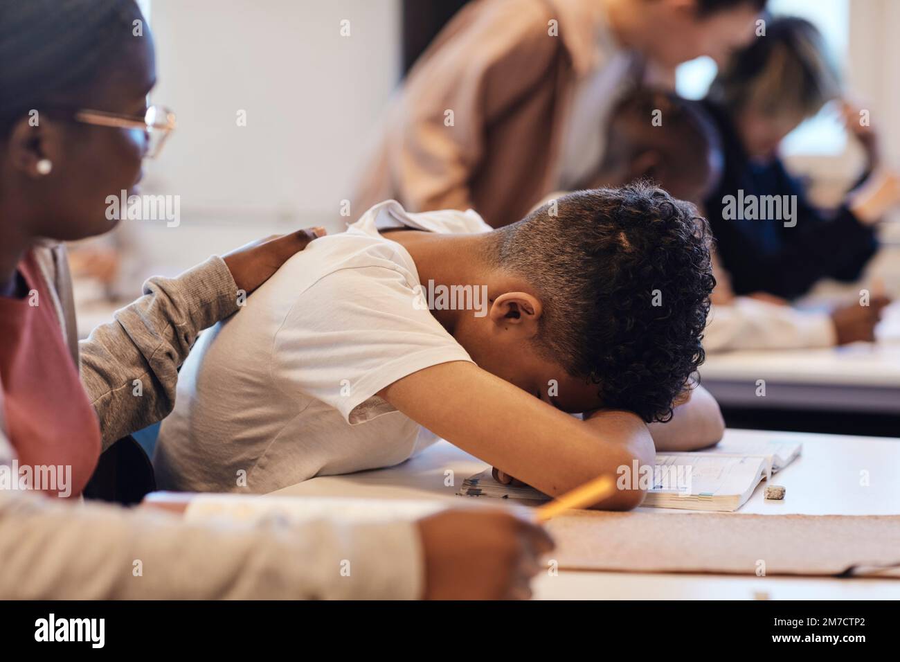 Female student consoling depressed teenage boy resting head on desk in classroom Stock Photo