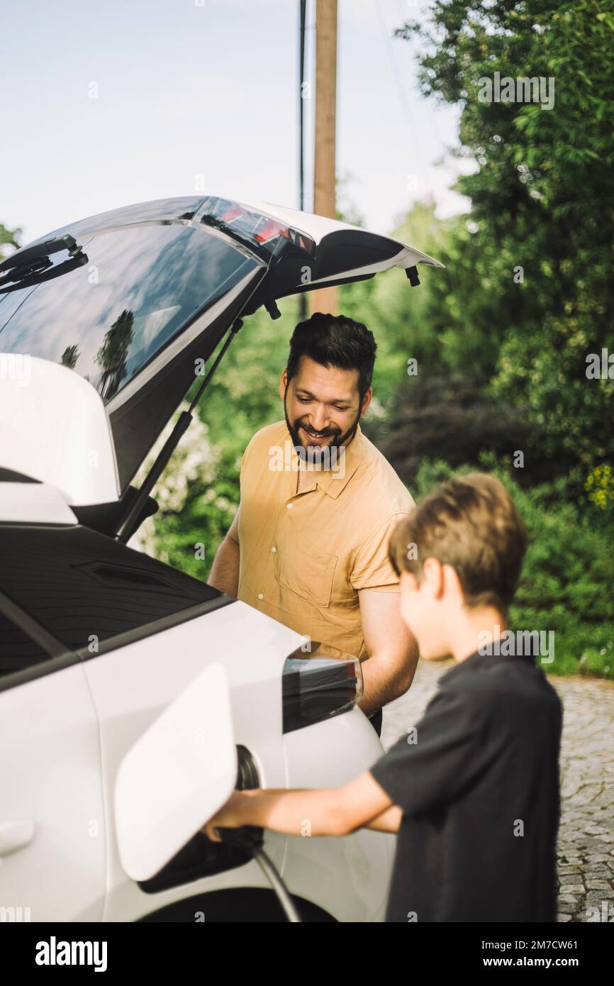Smiling father standing by son charging electric car Stock Photo Alamy