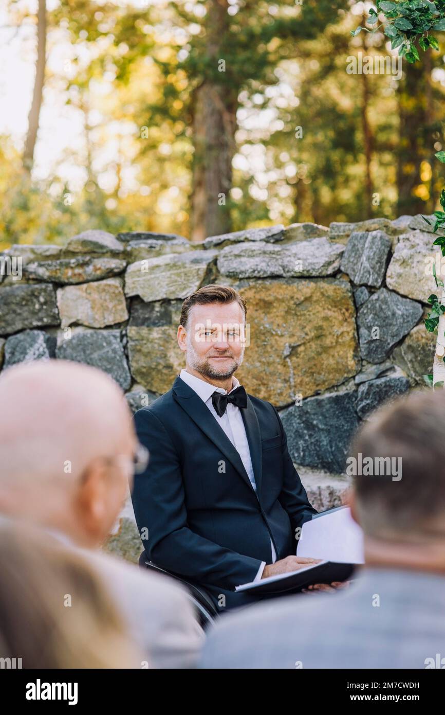 Minister holding book against wall looking at guests in wedding Stock Photo