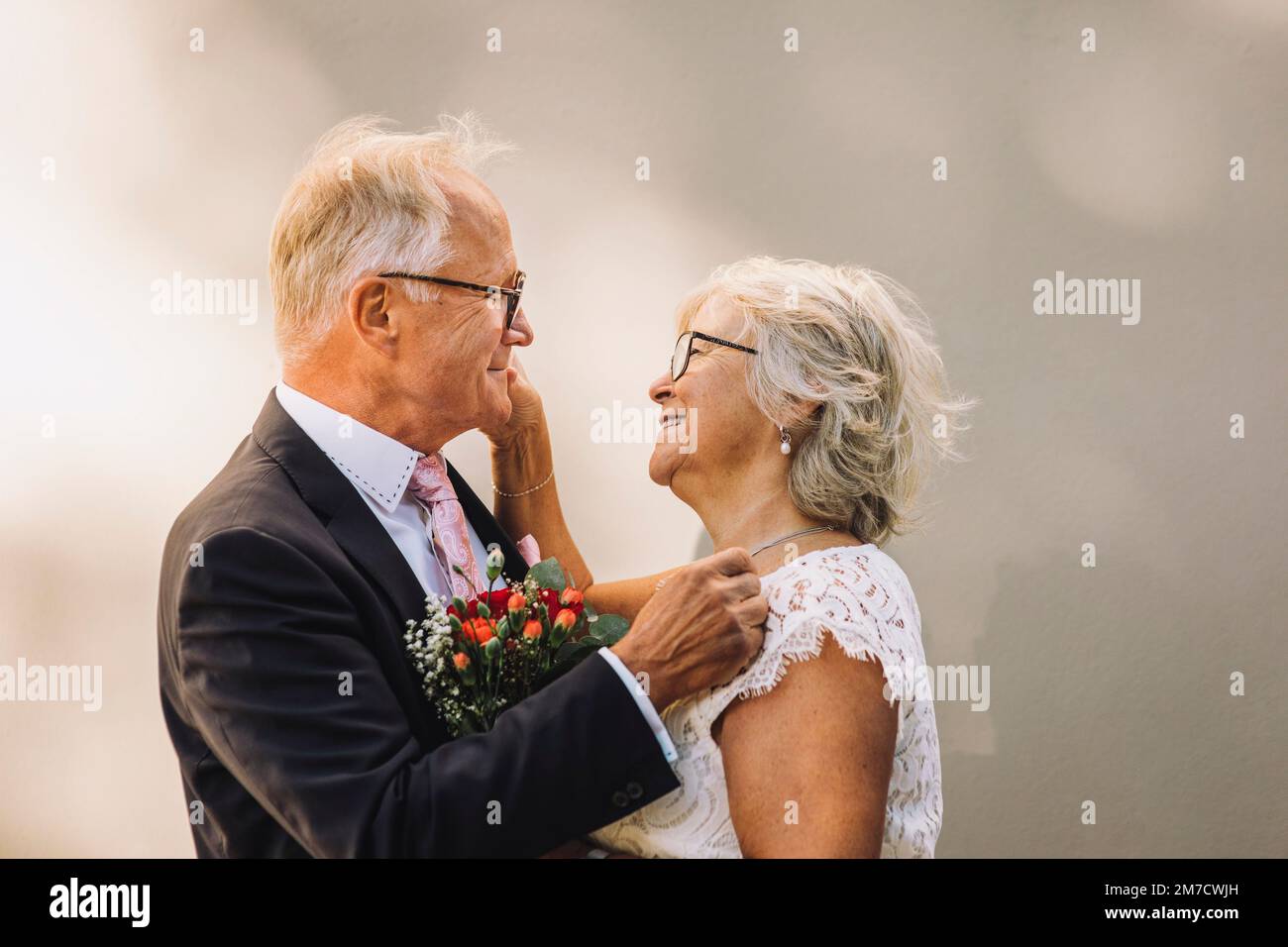 Side view of smiling senior couple looking at each other standing against wall Stock Photo