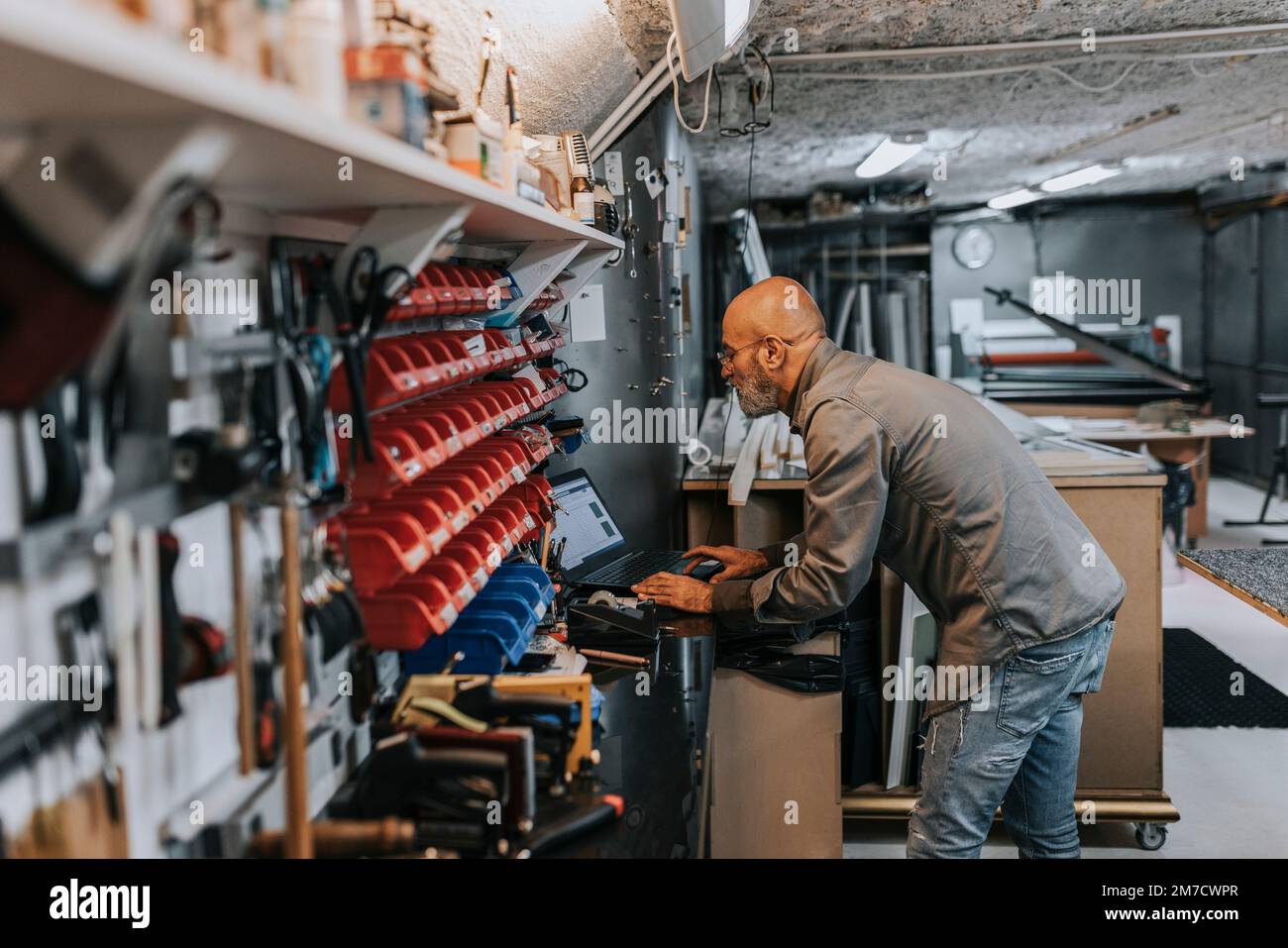 Bald male owner using laptop while working in workshop Stock Photo