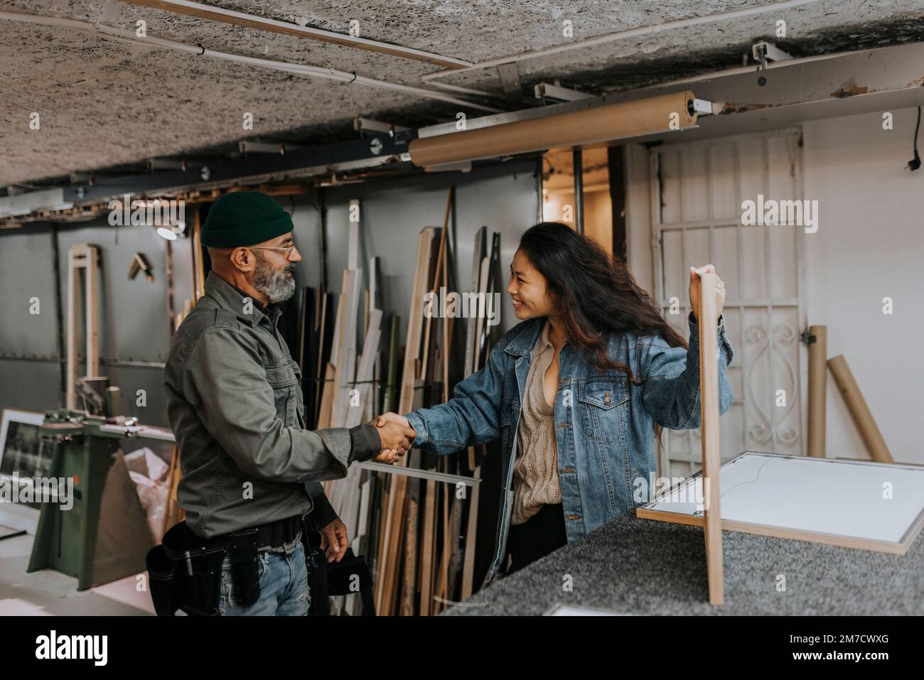 Smiling young woman shaking hands with craftsman in workshop Stock Photo