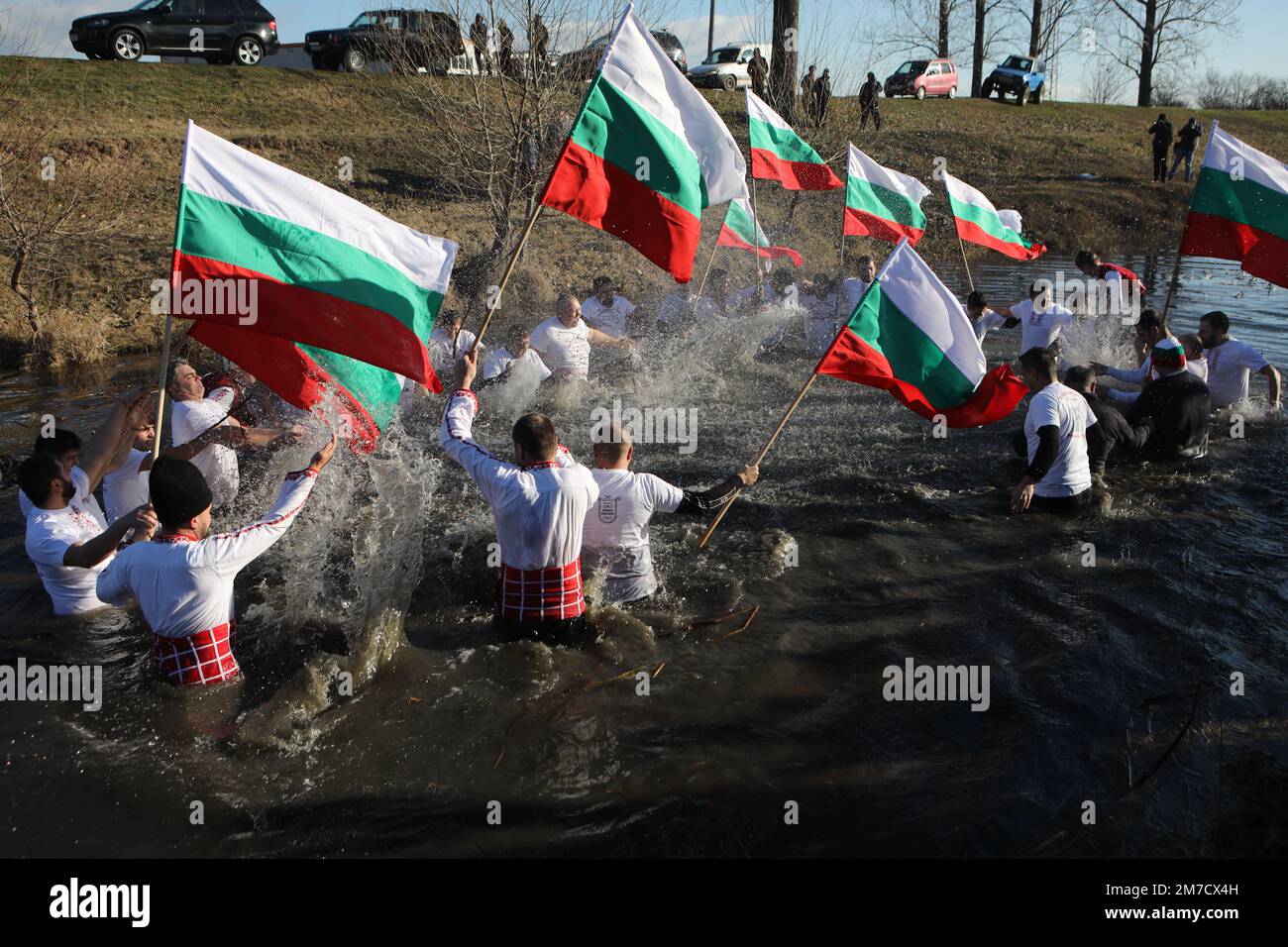 People perform the folk dance 'Horo' with national flags in the icy waters of Lesnovska River in Elin Pelin, during Epiphany celebrations Stock Photo