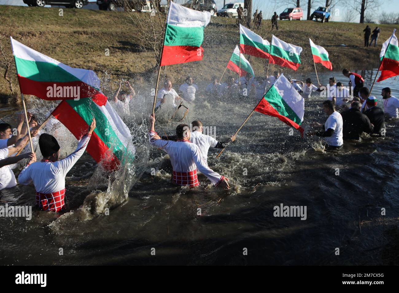 People perform the folk dance 'Horo' with national flags in the icy waters of Lesnovska River in Elin Pelin, during Epiphany celebrations Stock Photo