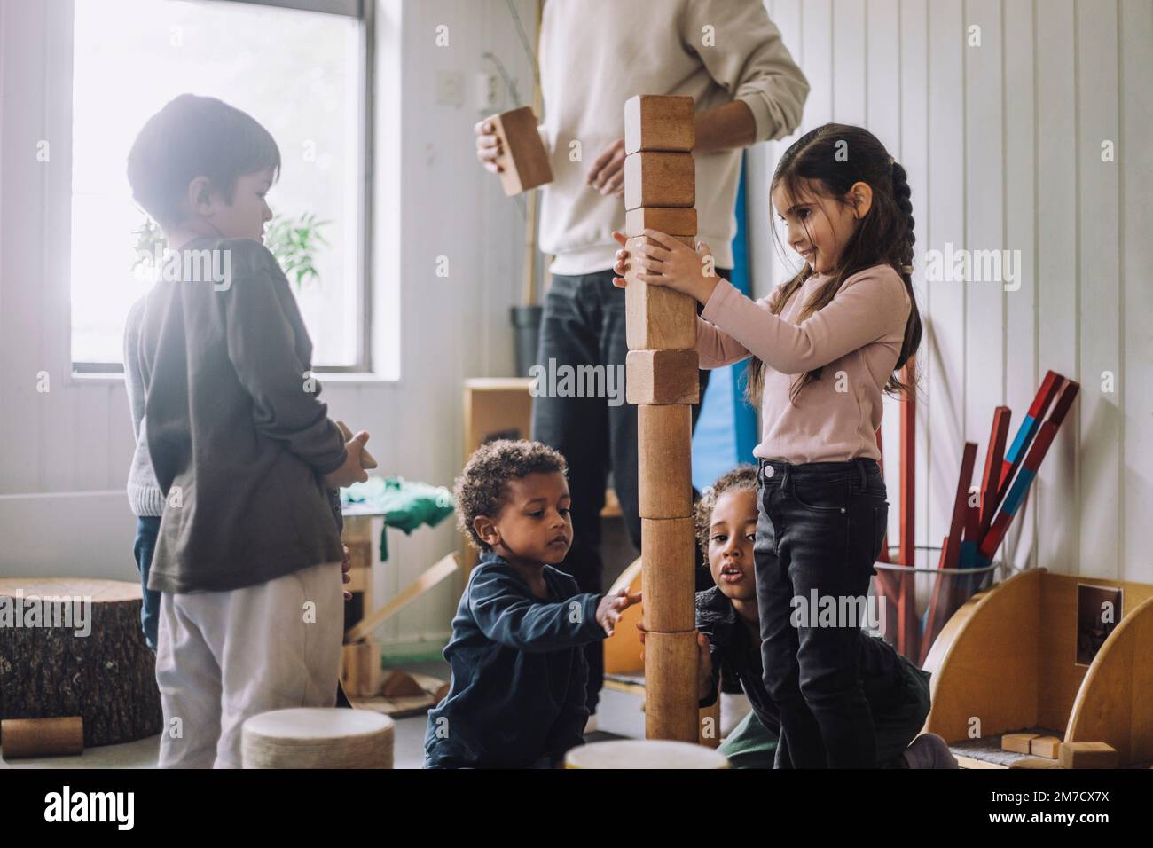 Female and male students stacking wooden toy blocks by male teacher in day care center Stock Photo