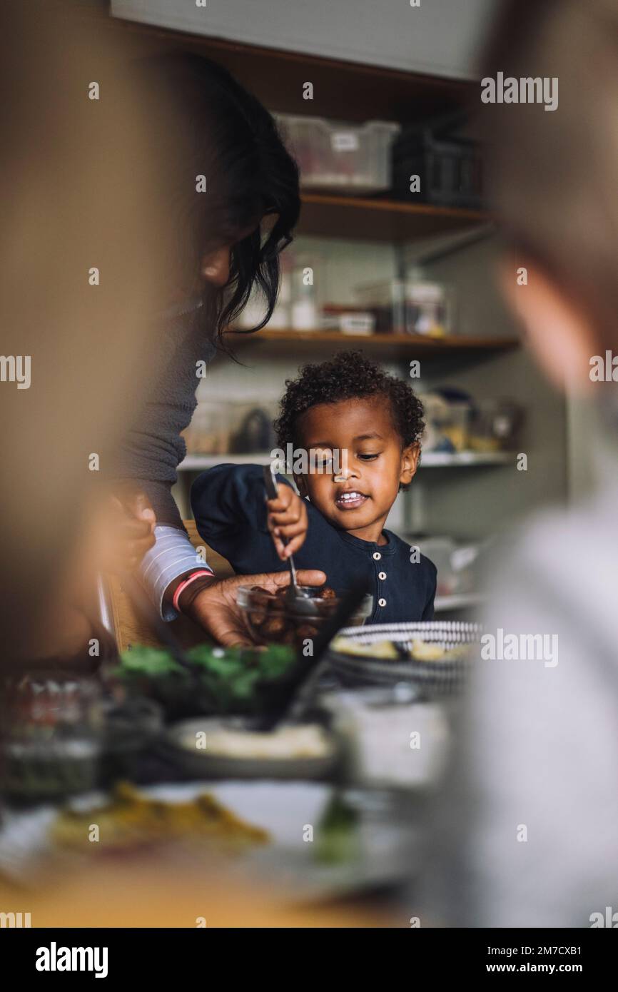 Female teacher serving food to boy while having breakfast in
