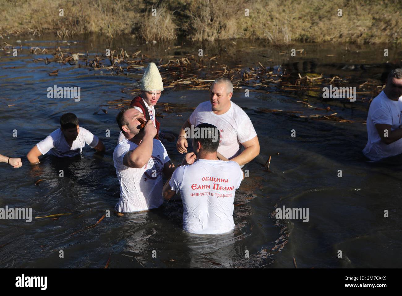 People perform the folk dance 'Horo' with national flags in the icy waters of Lesnovska River in Elin Pelin, during Epiphany celebrations Stock Photo