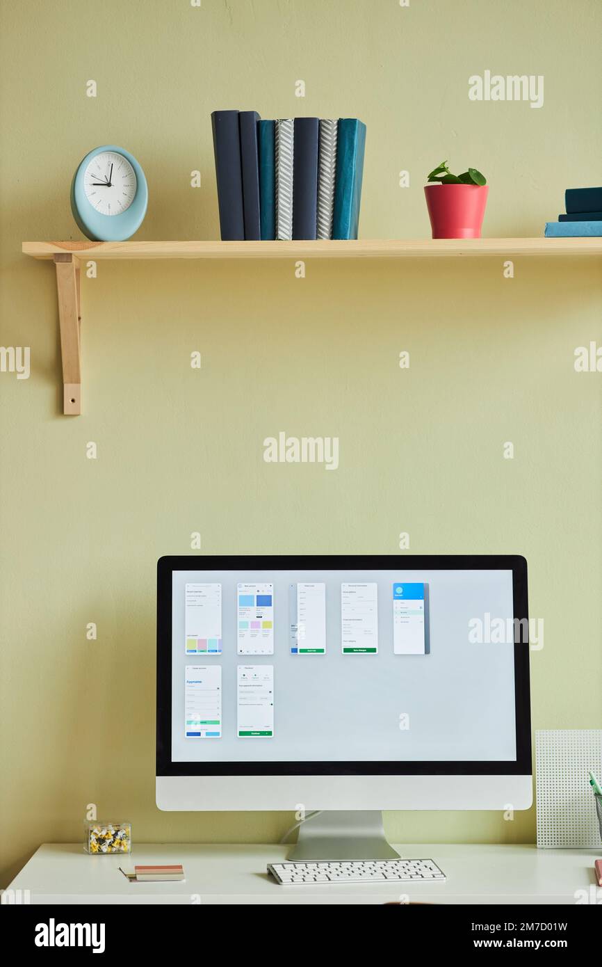 Vertical background image of minimal home office setup with computer screen and planning charts against pastel yellow wall Stock Photo